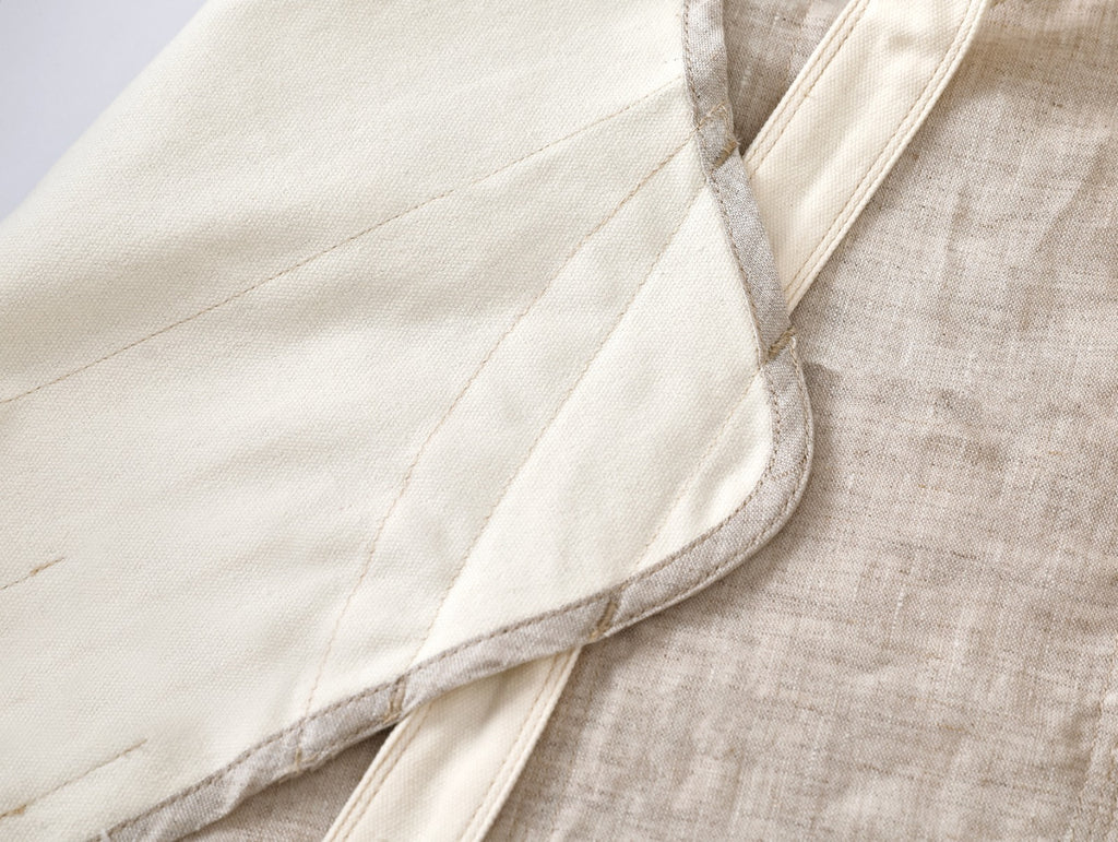 Close-up of a cream-colored quilted fabric panel with a stitched border, laid over a textured beige linen fabric.