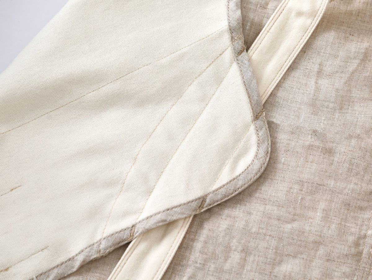 Close-up of a cream-colored quilted fabric panel with a stitched border, laid over a textured beige linen fabric.