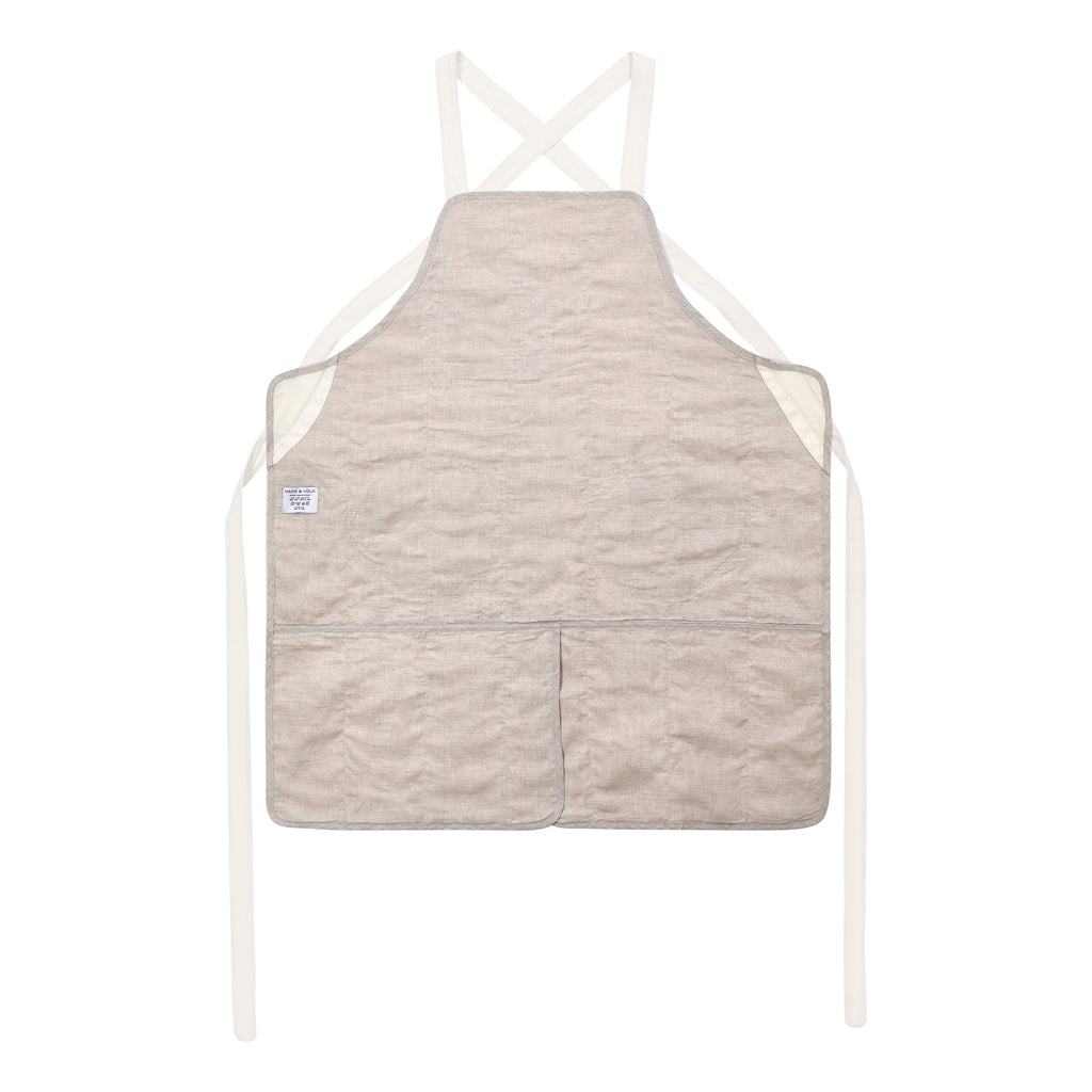 A light beige quilted chef apron with cream-colored straps and a small white brand tag on the left side, displayed against a solid white background.